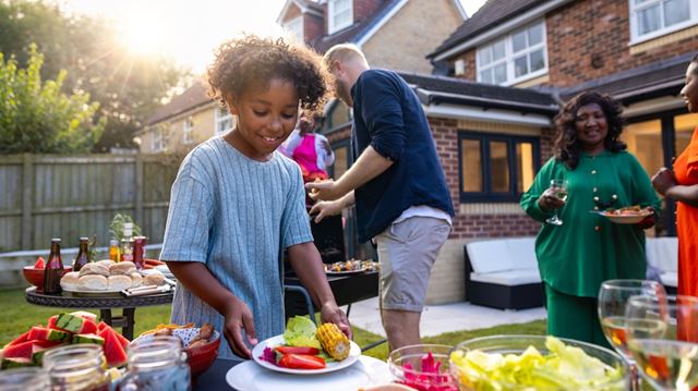 A child at a barbecue filling their plate with corn on the cob and other BBQ foods